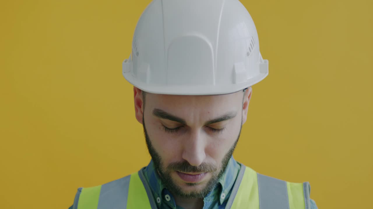 特写肖像的快乐的建筑工人在制服感动的安全帽和微笑的黄色背景视频素材
