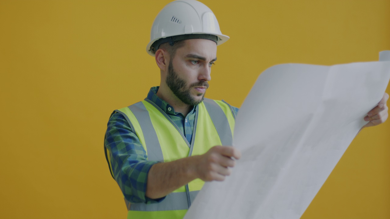 工业工程师看着蓝图，独自站在黄色背景上与队友交谈的慢动作。视频素材