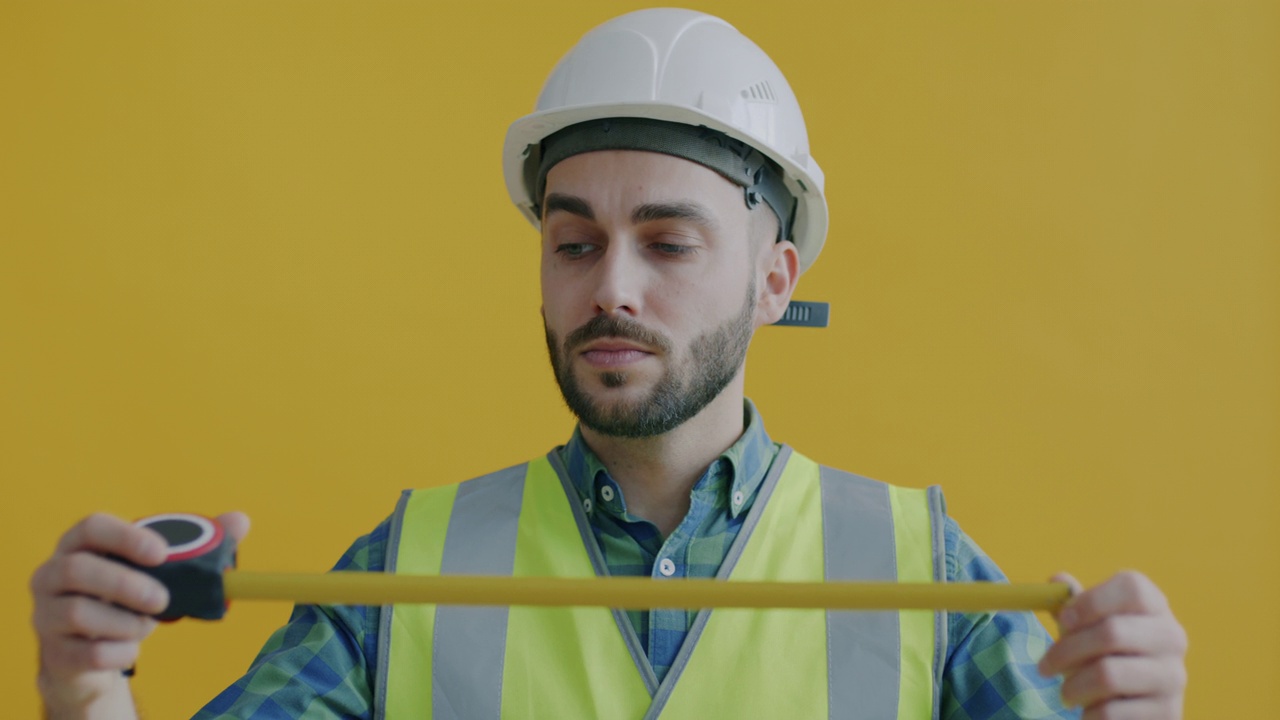 穿着制服的建筑工人像，用卷尺独自站在黄色背景上视频素材