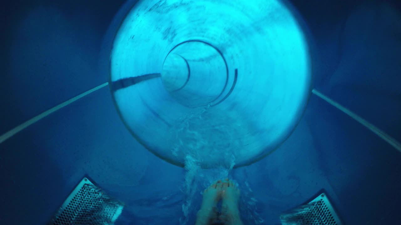 一个女孩在水上乐园里滑下一个封闭的蓝色管子。暑假的概念，旅行视频素材