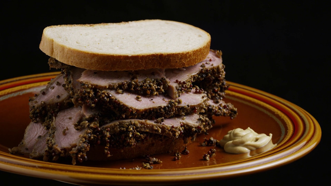 旋转拍摄的牛肉三明治与酱汁在盘子上，黑色哑光背景。视频素材