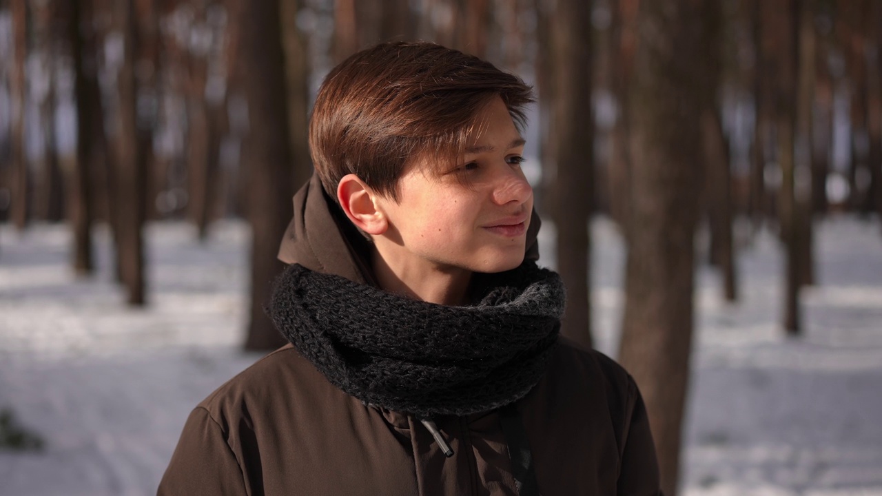 棕色眼睛的黑发少年站在阳光明媚的冬日森林里环顾四周。特写肖像的青少年高加索青少年享受生态旅游在户外度假。缓慢的运动。视频下载