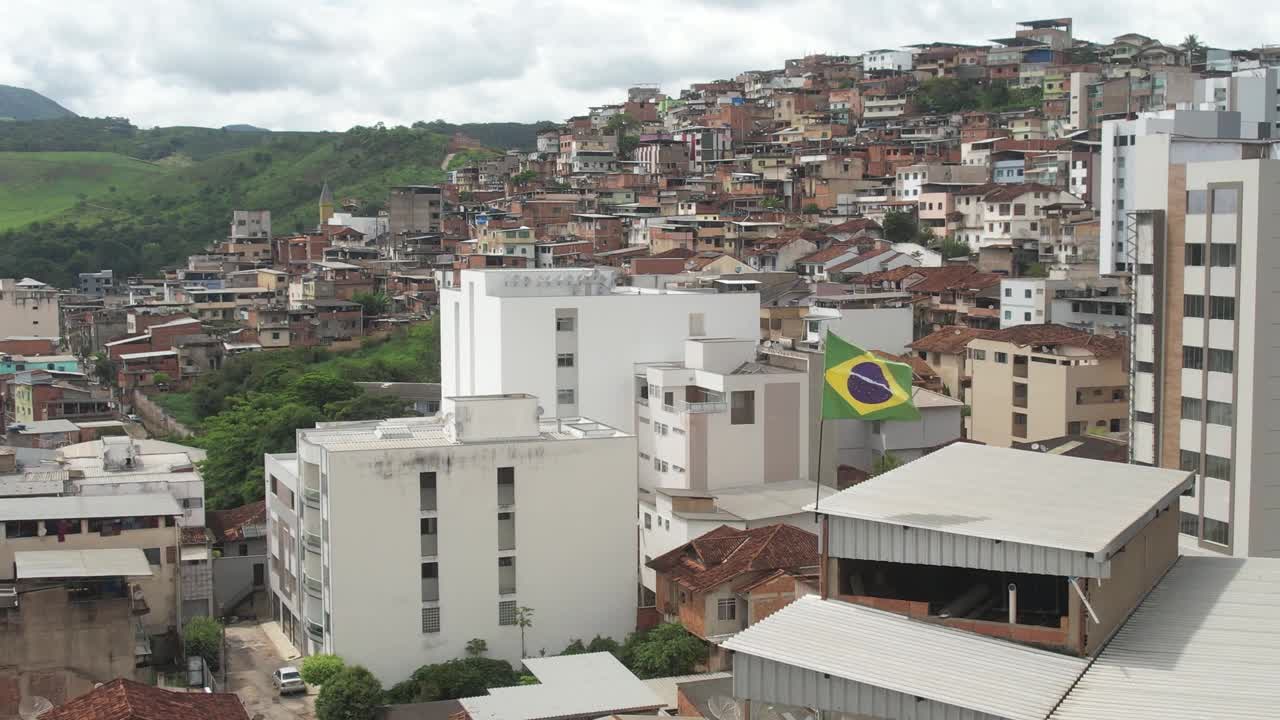 接近一面在风中飘扬的巴西国旗，背景是一个贫民窟视频下载