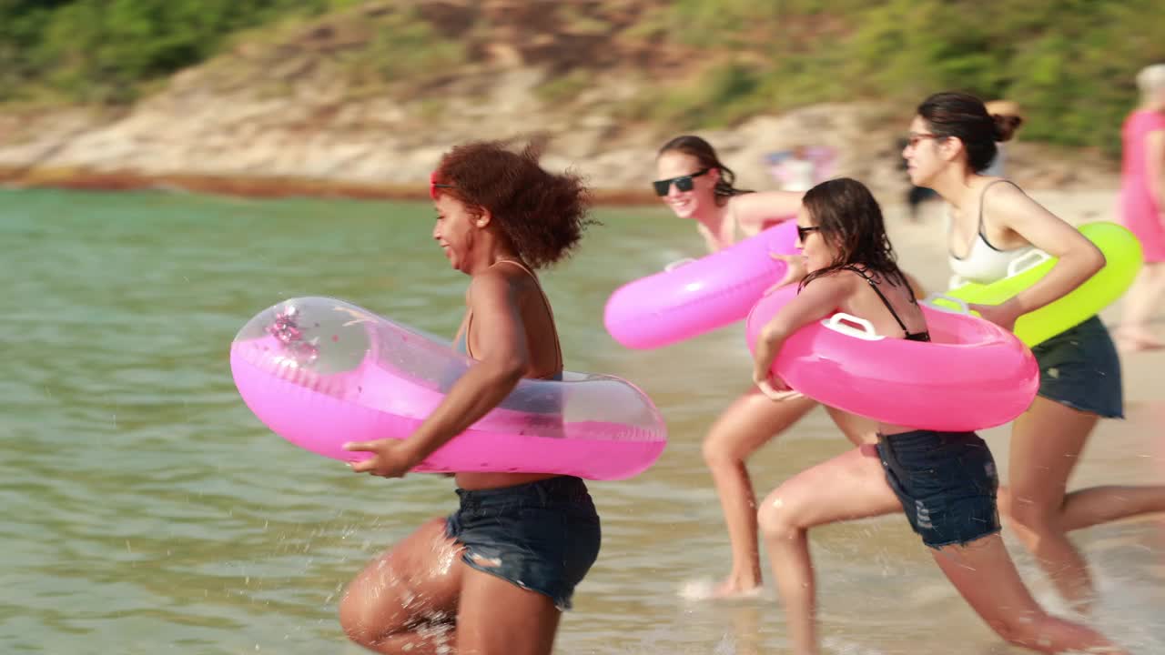 自由浮动。一群不同的少女在海滩上。四名少女在热带海滩上享受充气环。暑假旅行。视频下载