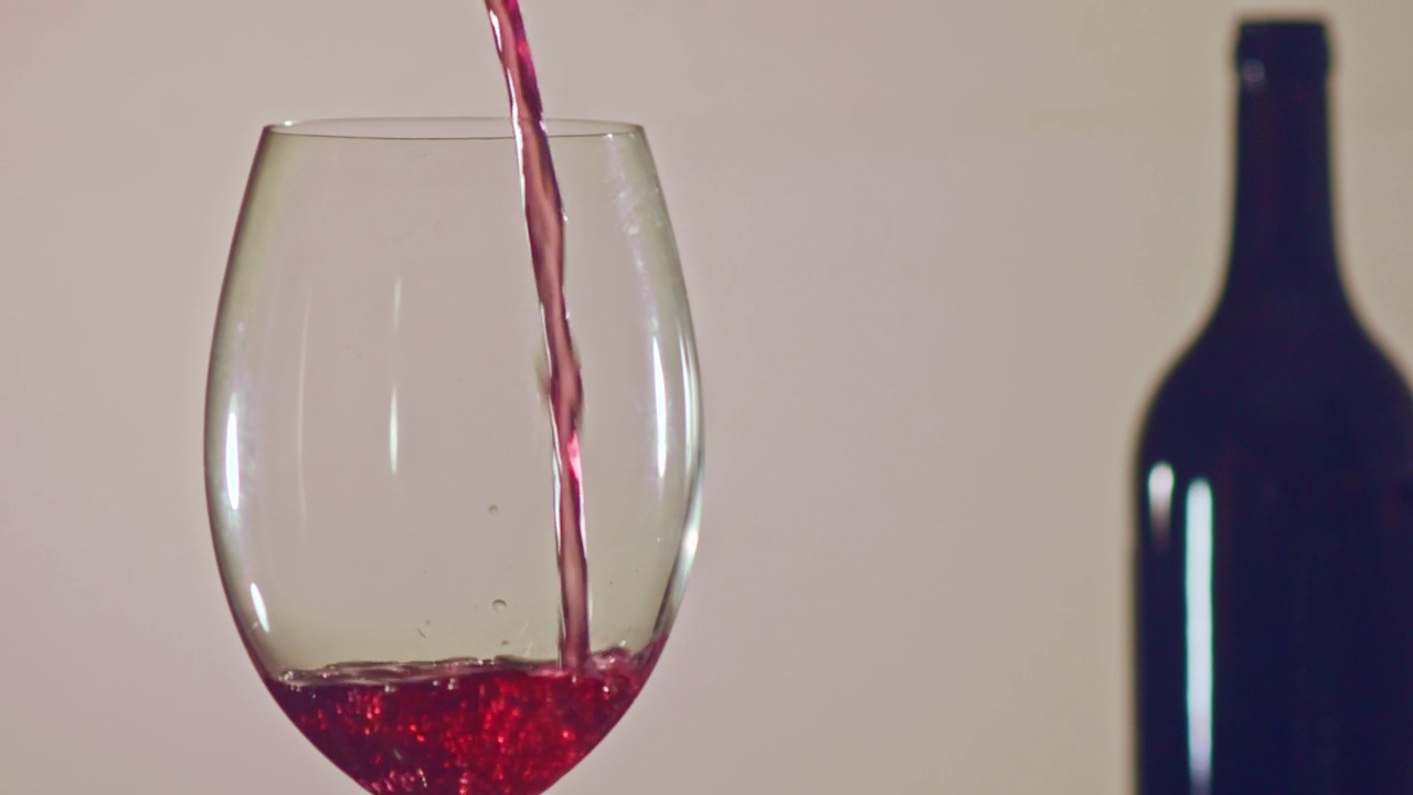 在中性的背景下，用酒瓶灌满一杯红酒——特写视频下载