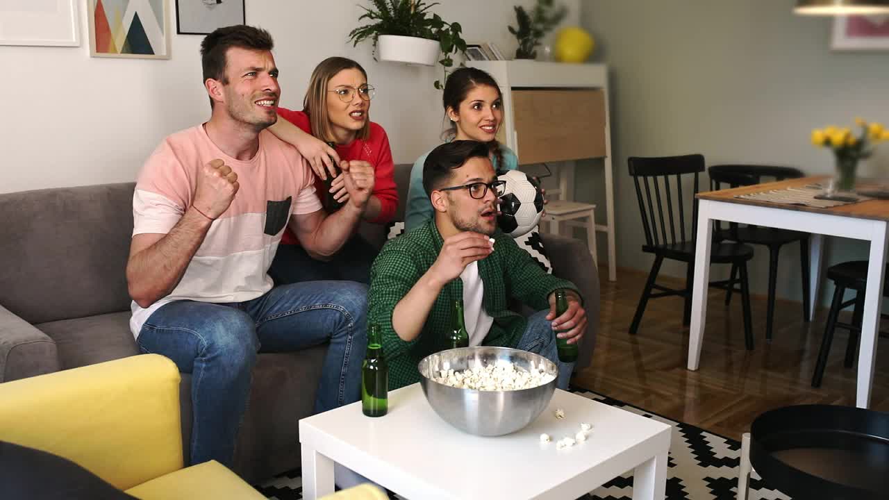 一群兴高采烈的朋友在家观看足球比赛，庆祝胜利。视频下载