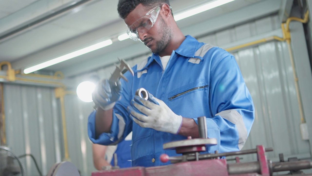 专业的黑人男性技术工人和同事在工厂车间使用游标卡尺测量机器零件的尺寸。视频素材
