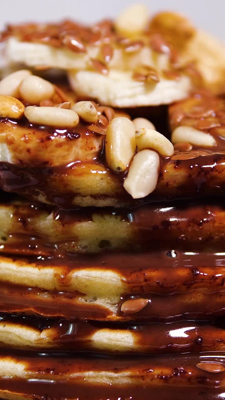 竖屏:巧克力糖浆的甜煎饼。在家烹饪的健康烧烤食物。美味的早餐，香蕉，坚果和巧克力。为社交媒体拍摄视频下载
