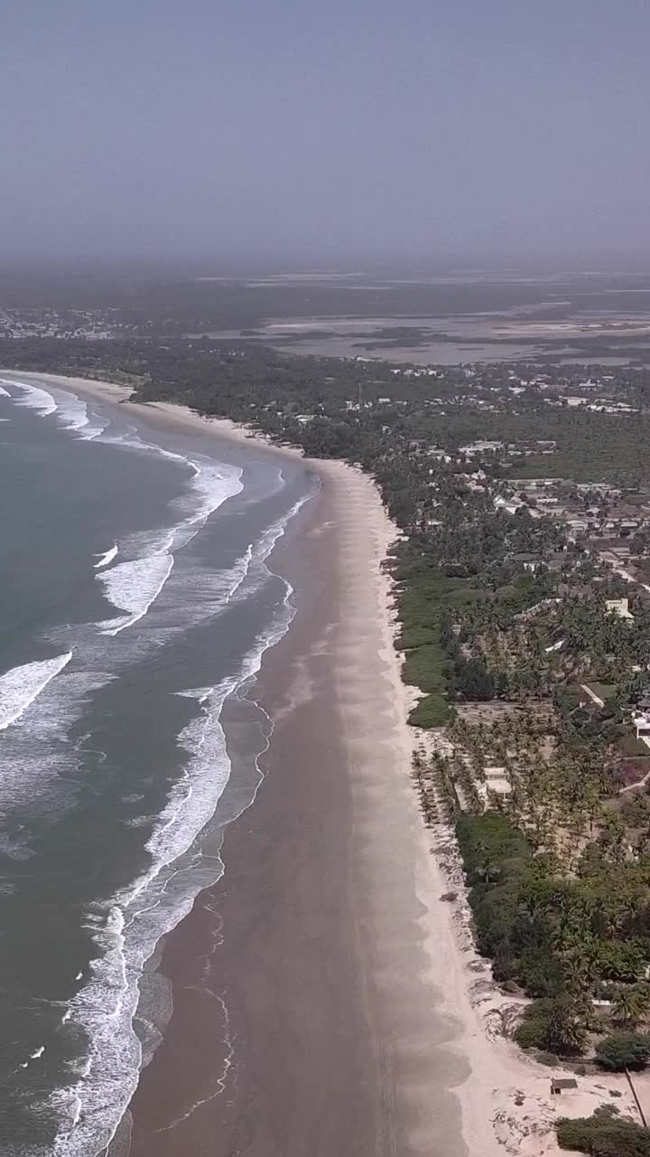 巨大的沙滩与海浪碰撞的垂直视频，沿海岸的植被和建筑物视频下载