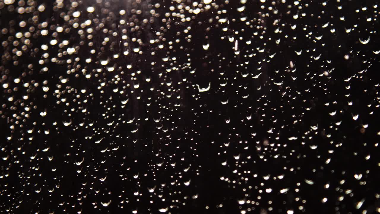 天气预报的镜头。雨滴顺着窗玻璃流下来。黑色背景与各种大小的发光球流动下来视频素材