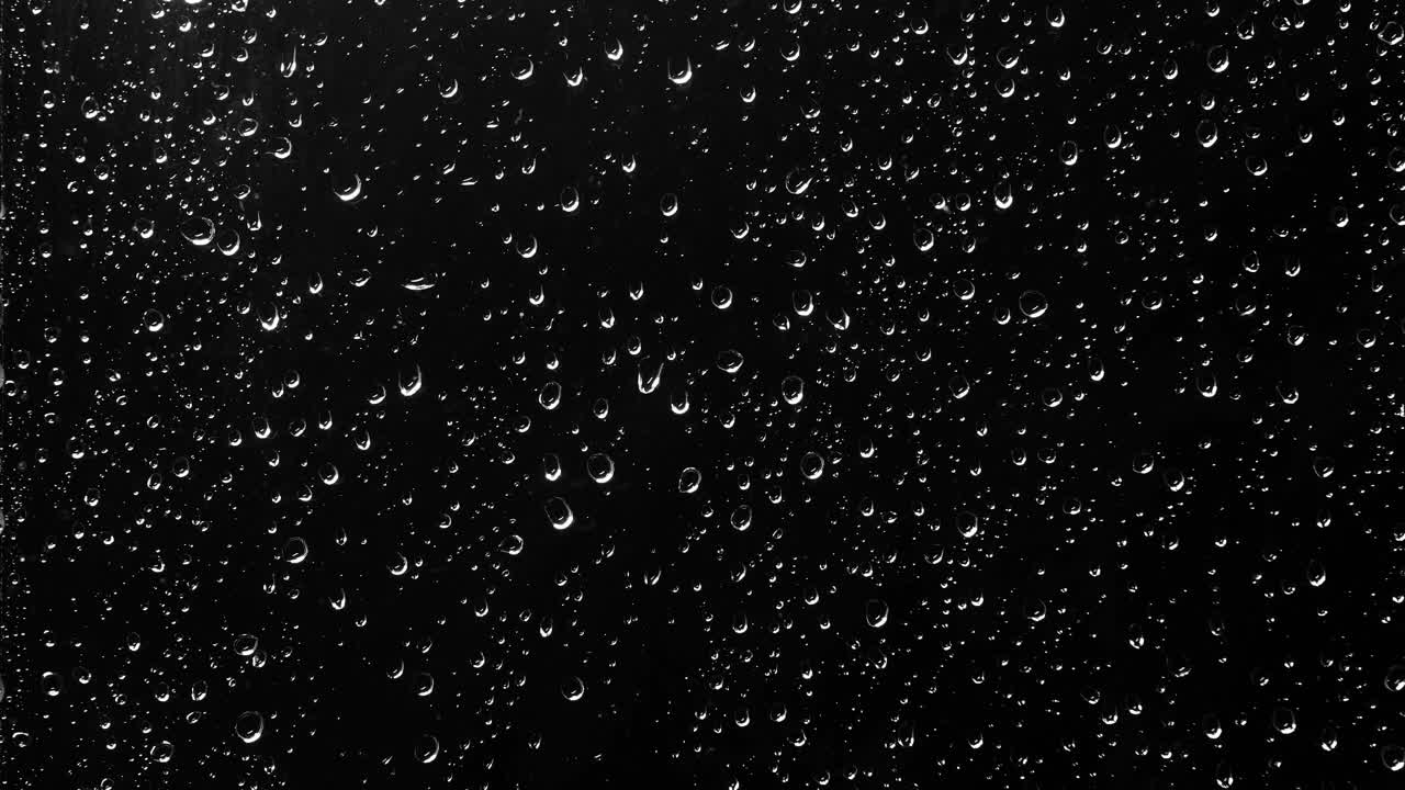 雨滴顺着窗玻璃流下来。黑色背景与各种大小的发光球流动下来视频素材