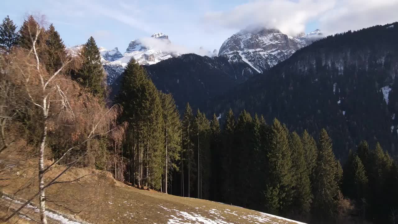 无人机在瑞士阿尔卑斯山脉中心的常绿松林上空飞行，令人惊叹的高岩山全景，山顶被雪覆盖，蓝天与山峰之间的地平线，云触摸山顶。瑞士的自然之美视频下载