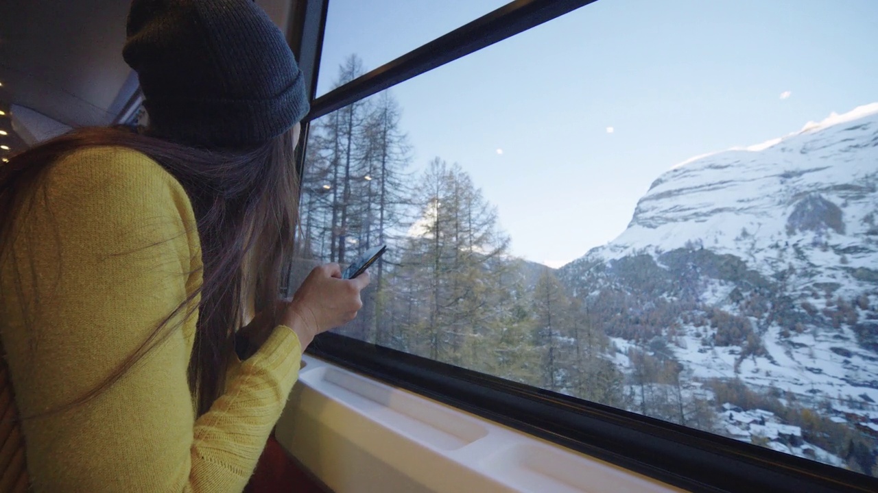 旅行的年轻女性坐在窗边，用手机乘坐火车前往瑞士采尔马特马特峰。多元理念的体验式旅行。与α。视频下载