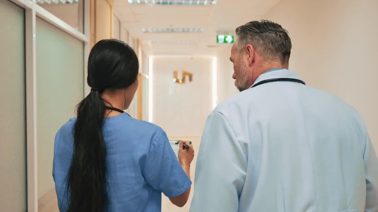 亚裔年轻护士与中年白人医生在医院走廊散步时讨论病人的情况。视频素材
