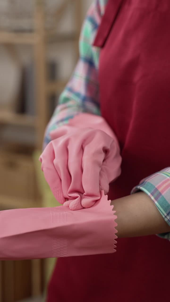 竖屏:妇女在做家务前戴着保护性橡胶手套。专注于女仆的手在准备打扫房间时戴上粉红色的手保护。视频素材