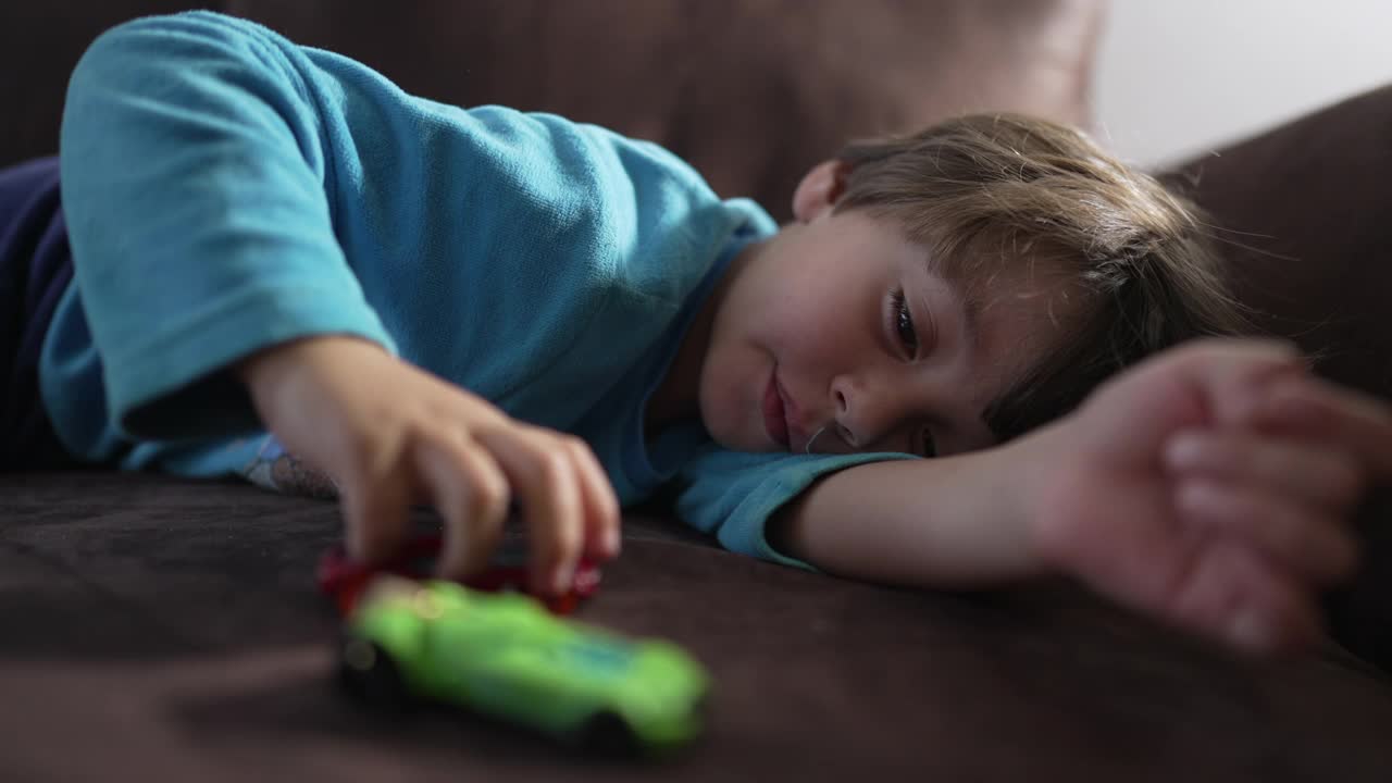 一个悲伤的孩子躺在沙发上玩玩具发呆。有消极情绪的无聊孩子视频素材