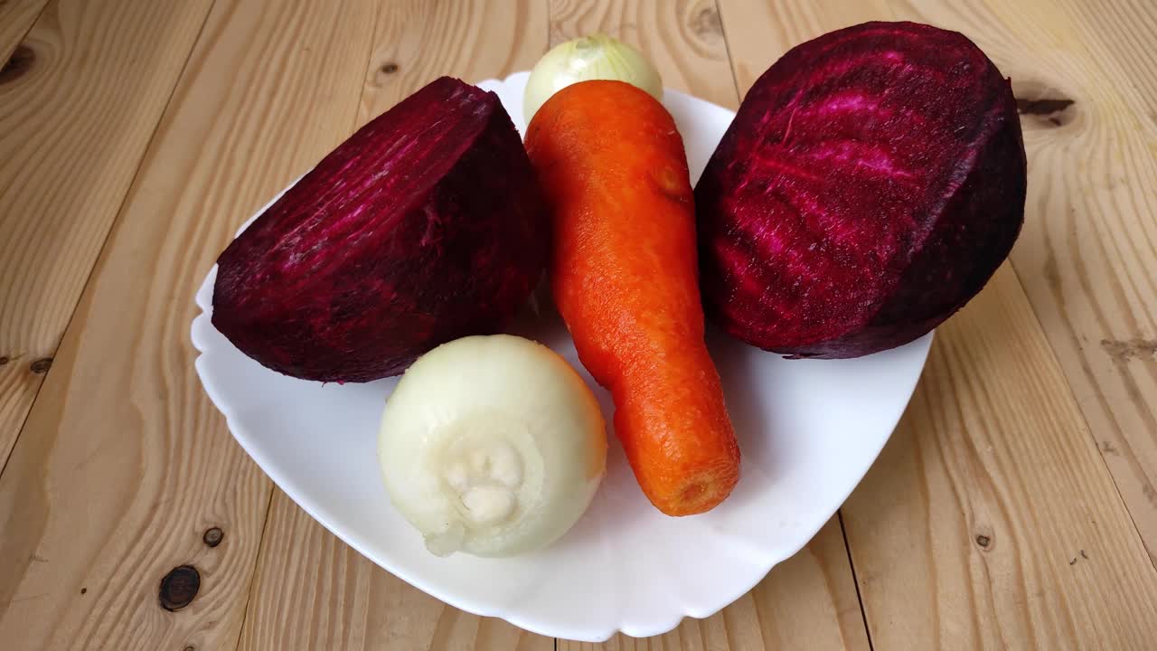 桌上有一个盛着蔬菜的盘子。红色甜菜根、胡萝卜和洋葱轮流放在白色盘子上。准备在厨房做饭。视频素材