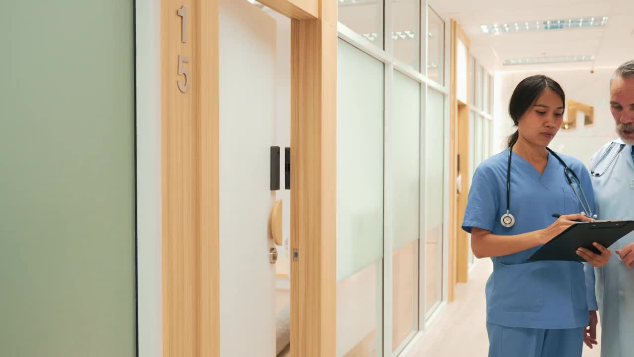 年轻的亚裔护士正在向中年白人医生咨询一个病人的情况。视频素材