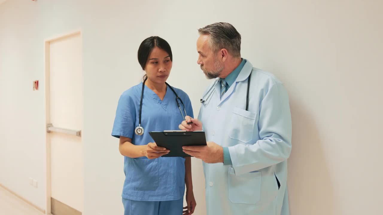 年轻的亚裔护士正在向中年白人医生咨询一个病人的情况。视频素材