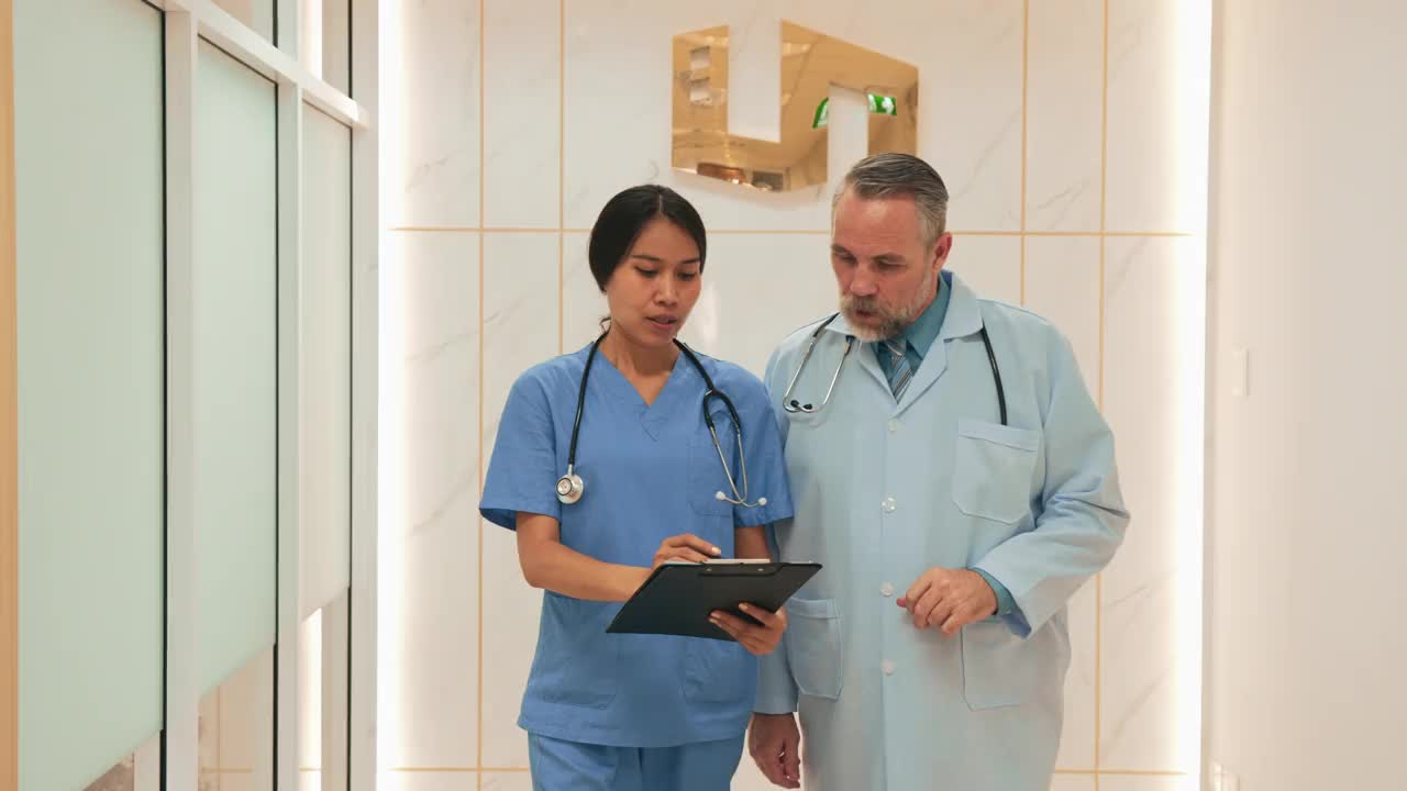 在医院的走廊里，亚裔青年护士正在和中年白人医生讨论一个病人的情况。视频素材
