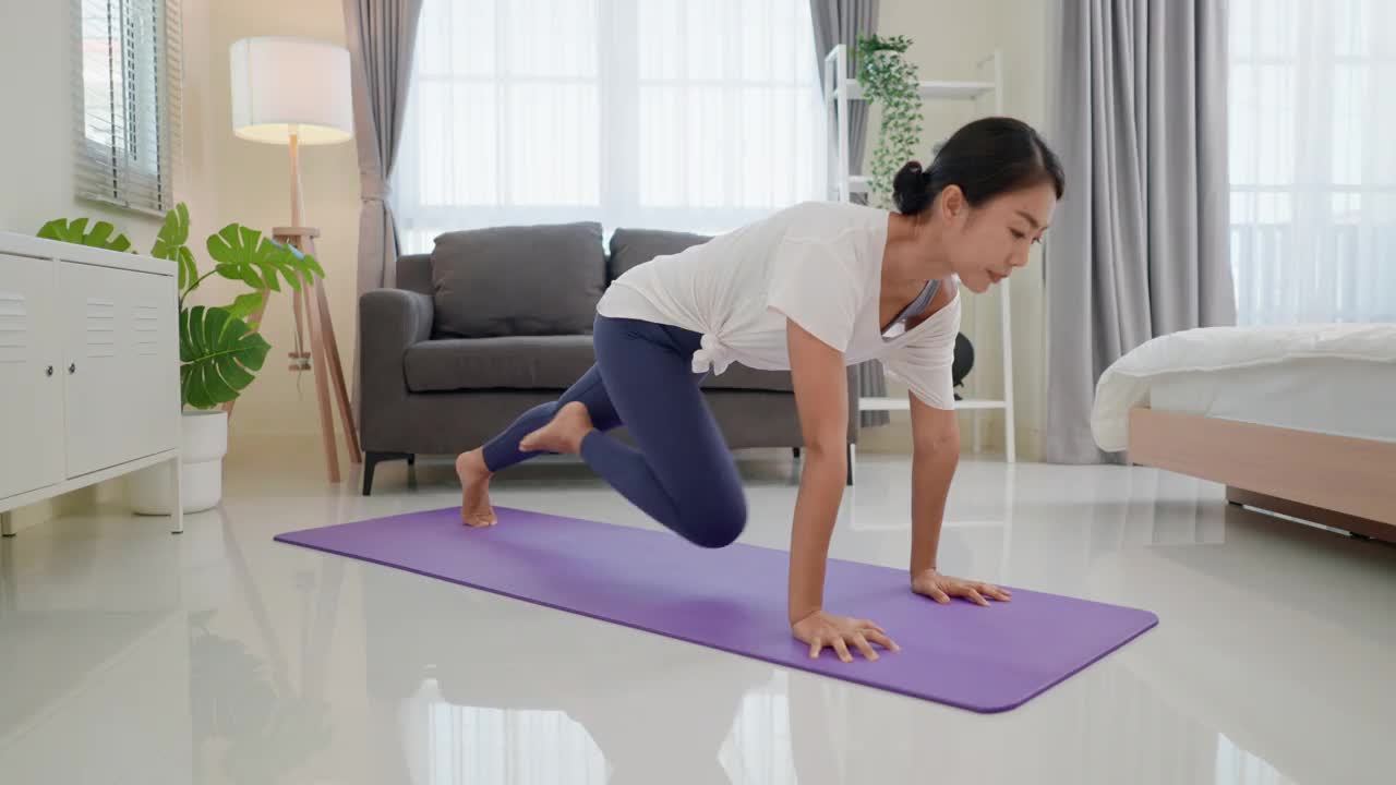 健康的年轻亚洲女子在白色和蓝色运动服练习初级瑜伽姿势调整身体平衡。她的手放在客厅的瑜伽垫上。家庭健身。视频素材