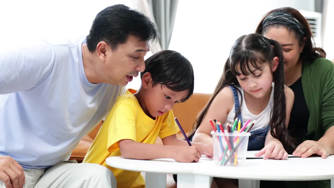 亚洲父亲和母亲看着孩子在家里画画。视频素材