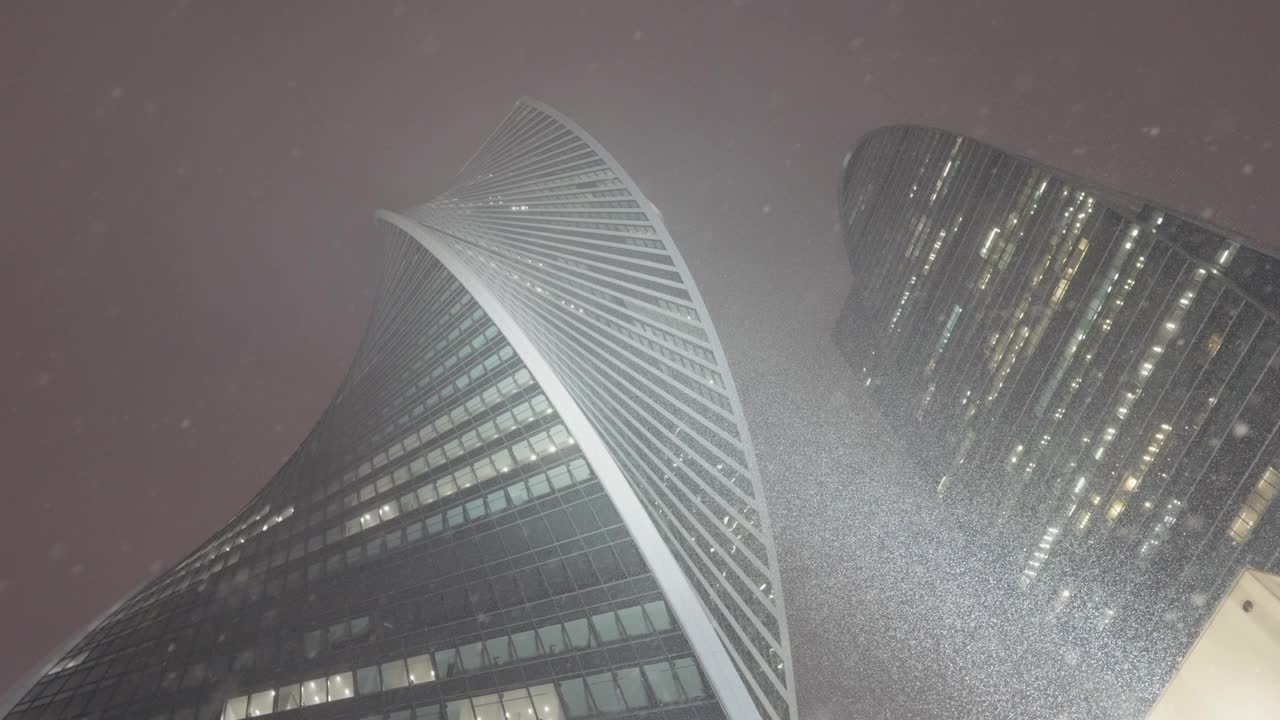 俄罗斯，莫斯科——2022年1月15日:夜晚降雪中的摩天大楼。行动。现代城市商业高层在冬季夜晚的底视图。美丽的摩天大楼和夜晚的降雪。莫斯科城市建筑视频素材