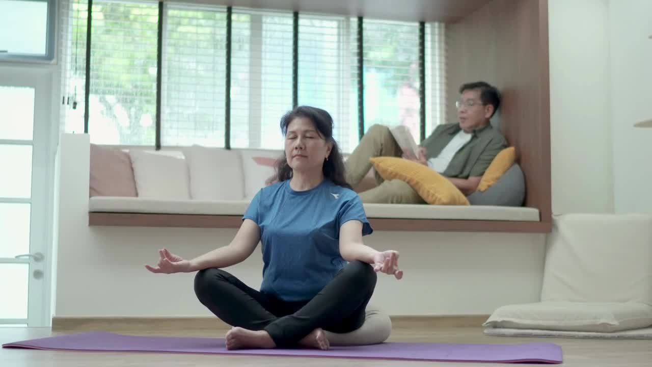 年长的亚洲夫妇在客厅看书和做瑜伽视频素材