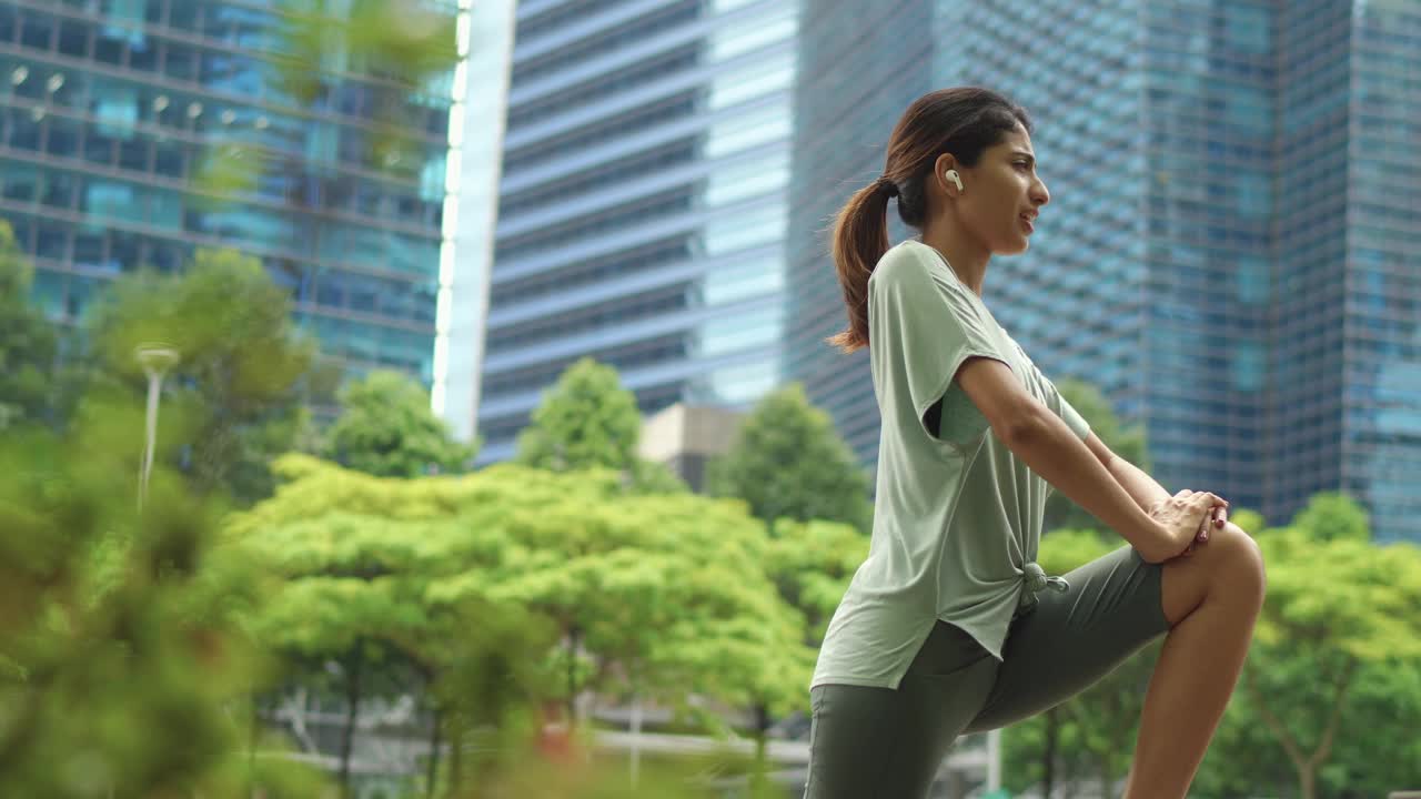 一名亚裔印度妇女在市中心做腿部伸展运动时看着手表视频下载