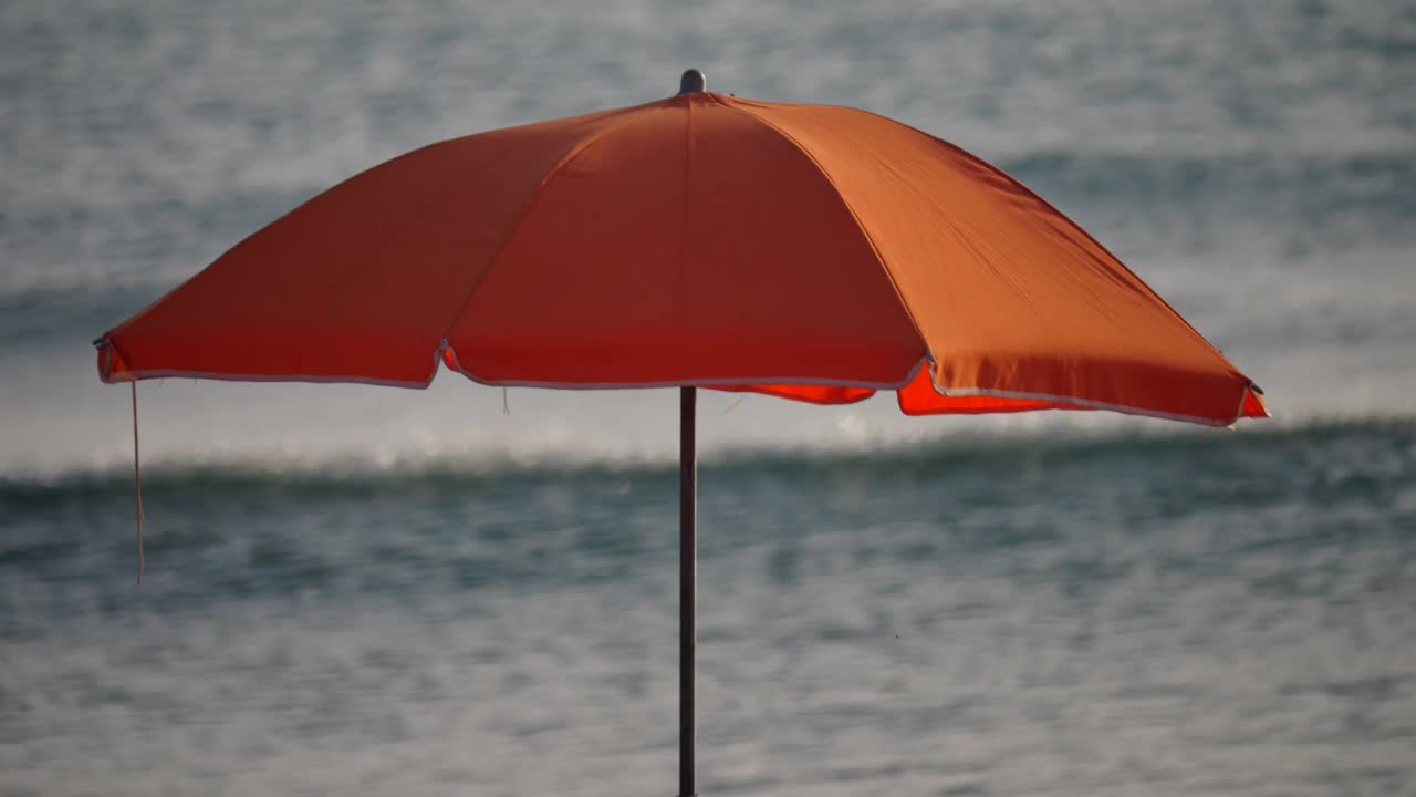 在慢镜头中，一把橙色的沙滩伞挡住了海浪。视频下载