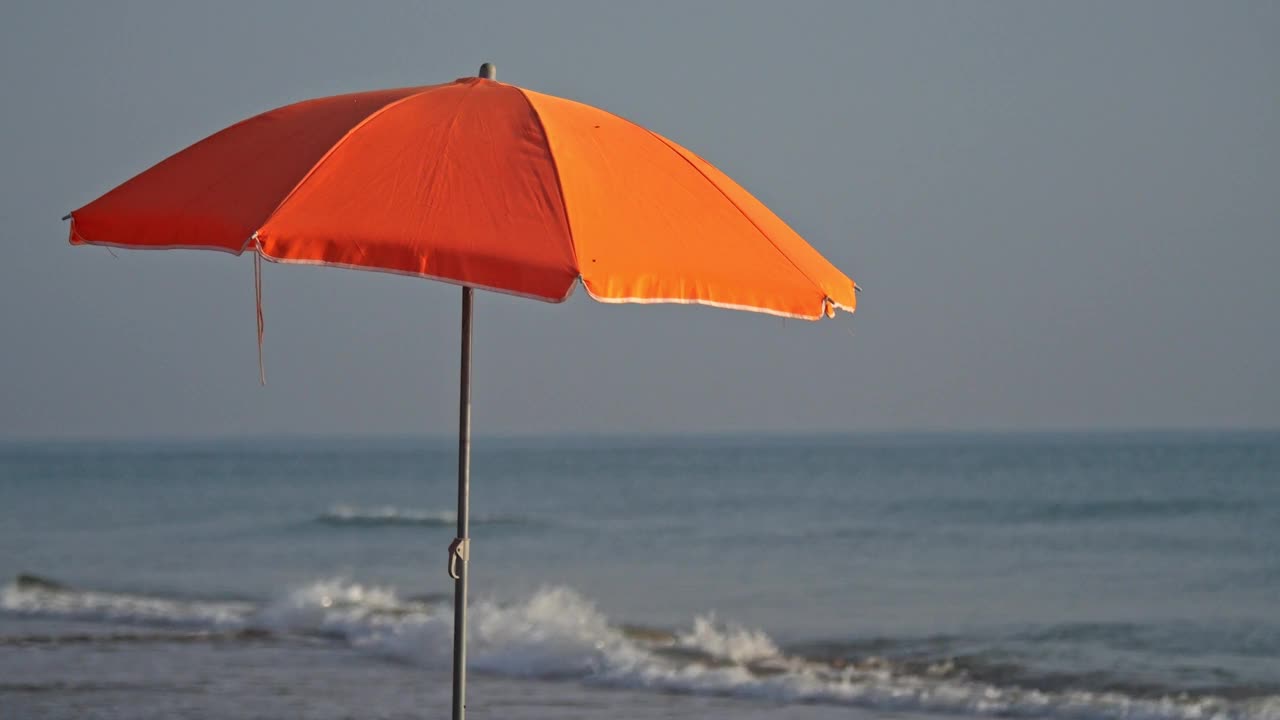 橙色沙滩伞遮挡着海浪，慢动作拍摄。视频下载