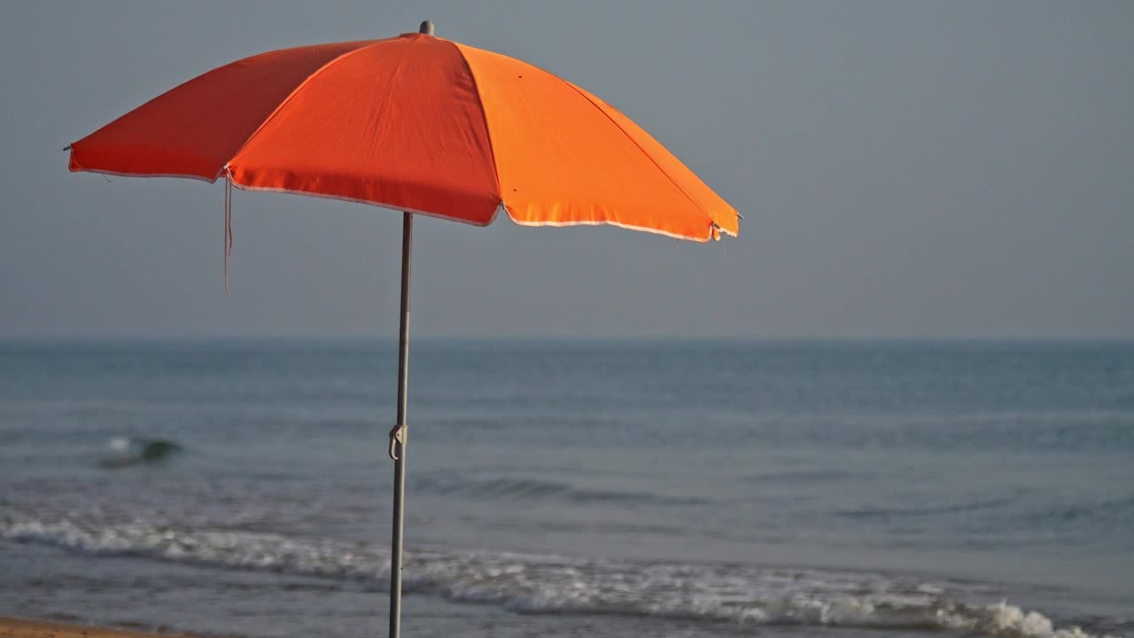 一把橙色的沙滩伞在海浪中缓缓移动视频下载