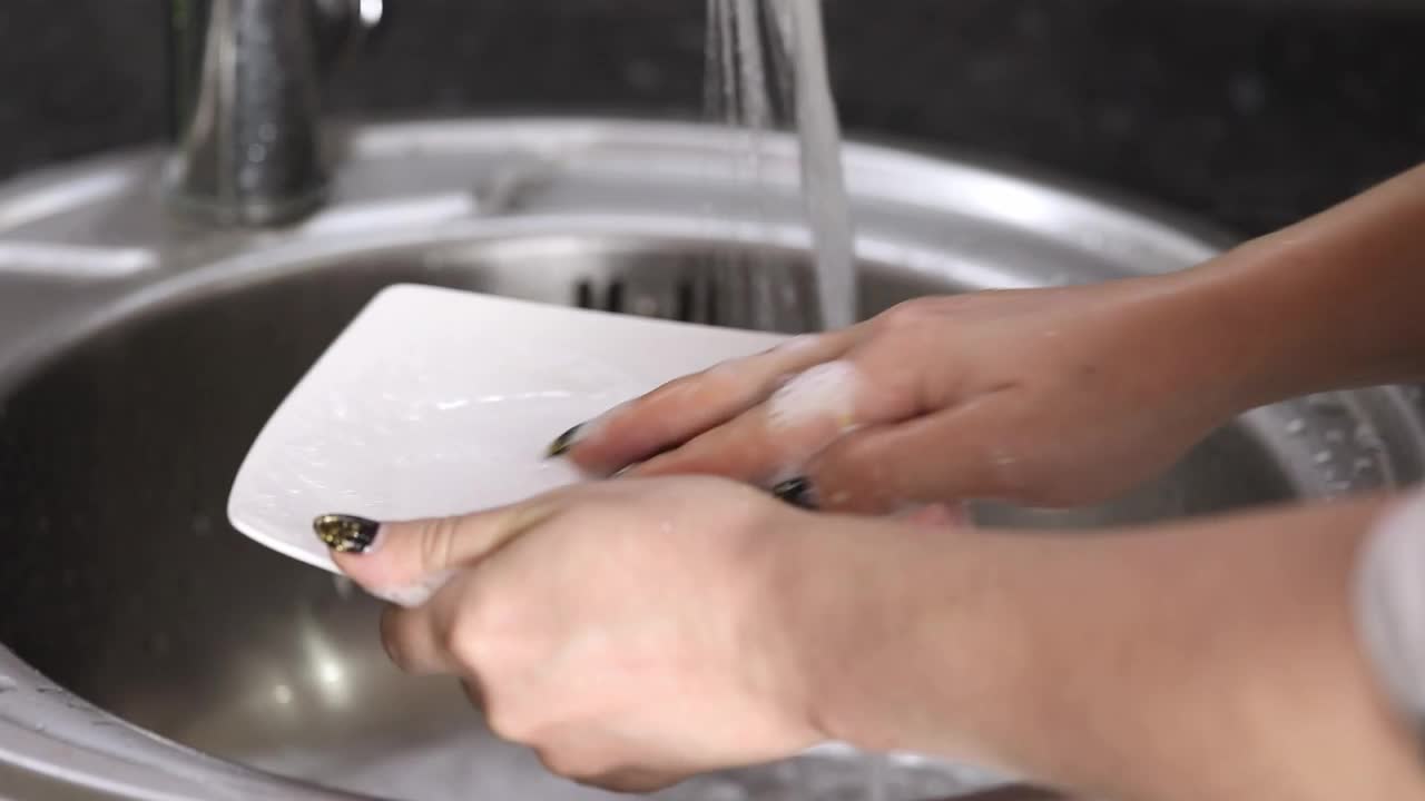 女性用自来水清洗带有泡沫的白色盘子视频下载