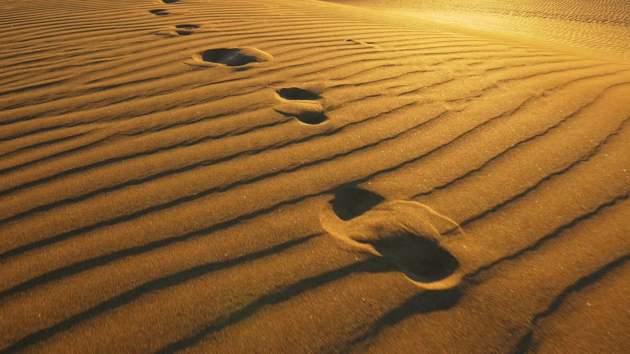摄像机追踪大沙丘上的脚印。温暖的夕阳下，沙漠里沙滩上的脚印。UHD 4 k视频下载