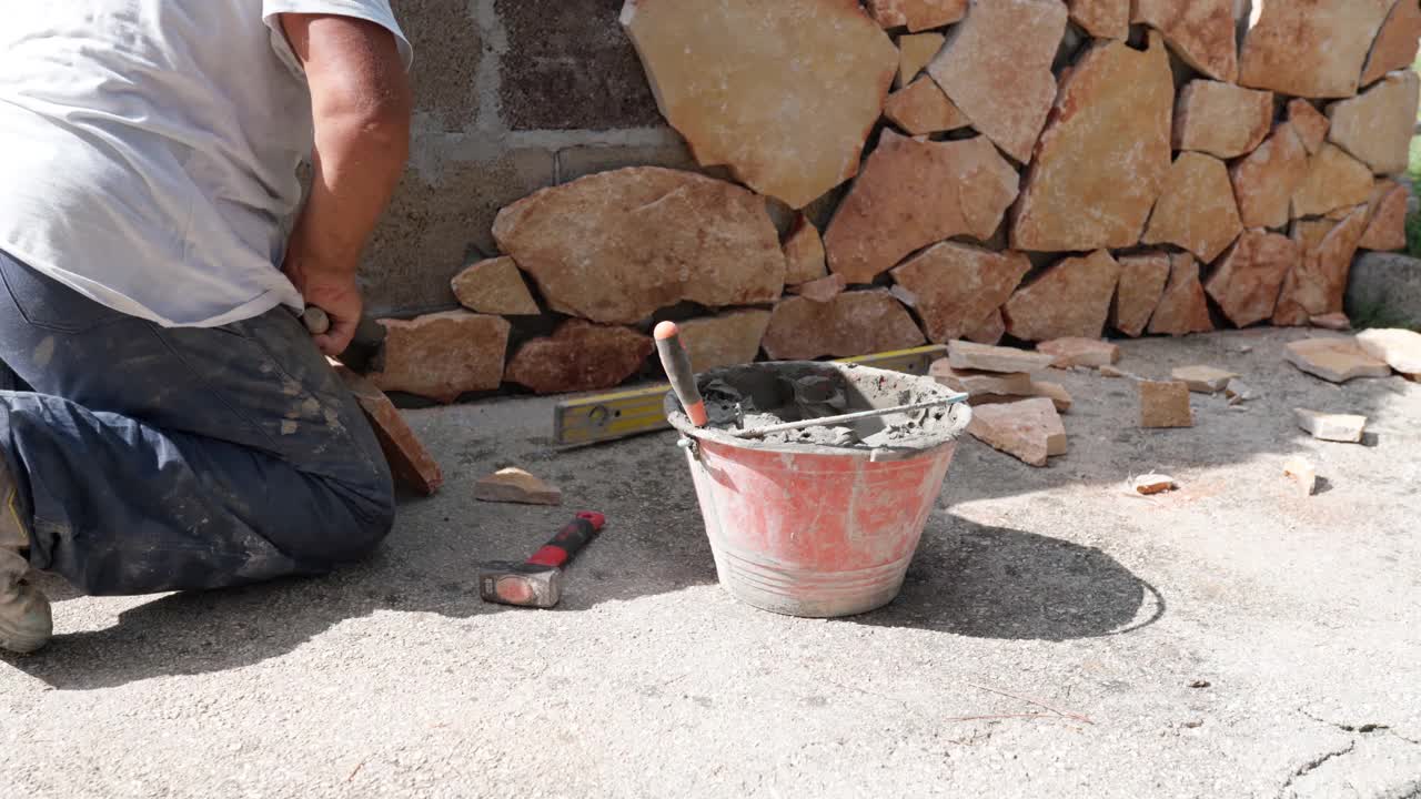施工人员在外墙安装装饰性的橙色岩石，工人将湿水泥溶液涂在石头上并贴在墙面上，施工现场砌砖视频素材