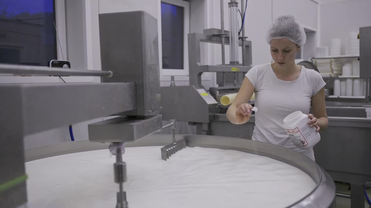 一名妇女在一个装满牛奶的大金属锅里加盐——在奶牛场工作视频下载