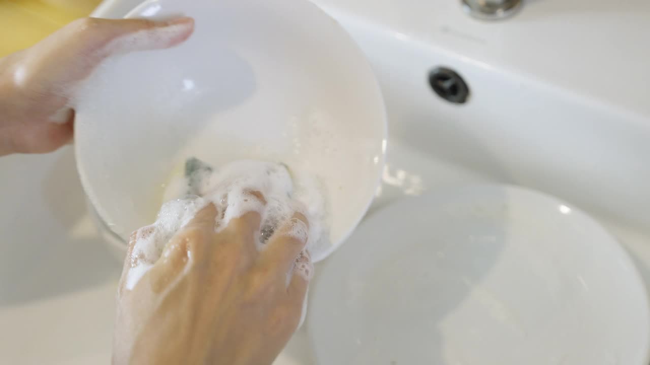 一位不知名的女性正在用洗洁精和柔软的清洁海绵清洗碗。视频下载