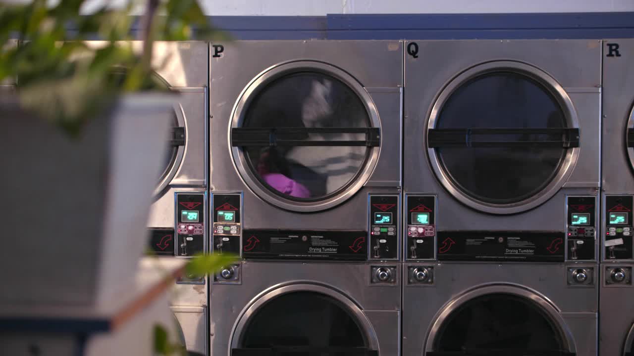 在自助洗衣店，一名男子把洗衣机装在一对母女旁边视频素材