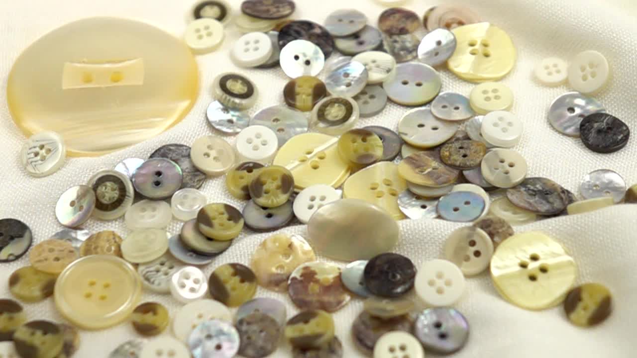 珍珠母钮扣落在白色的纺织背景上，慢动作视频下载
