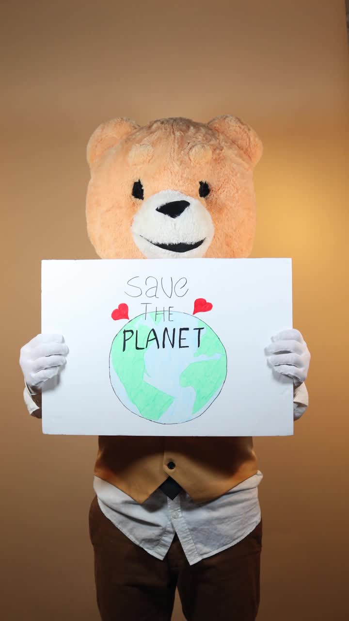 一名黄色背景泰迪熊头像的男子指着一个写着“拯救地球”的标志。社交网络的垂直视频视频下载