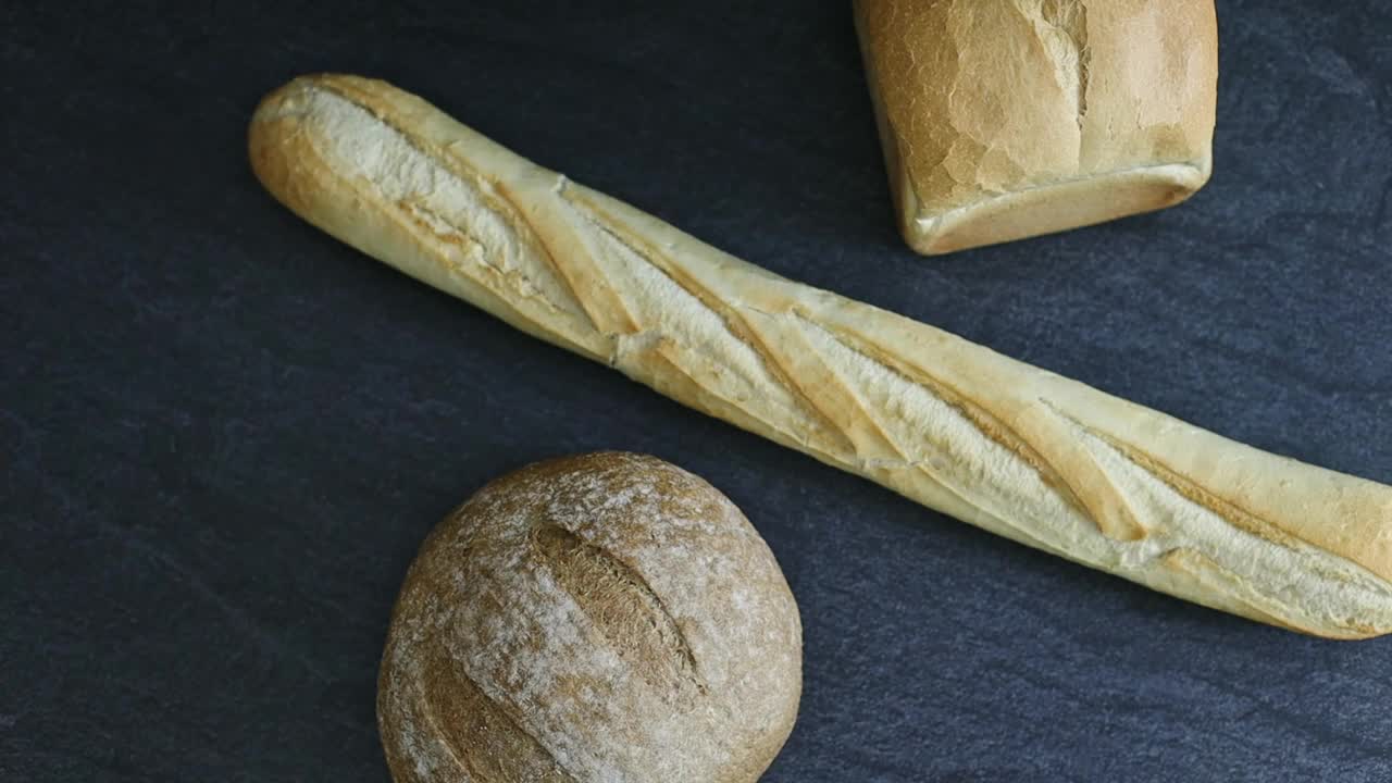 两个面包和一个法国法棍面包，黑色的石头背景。视频下载
