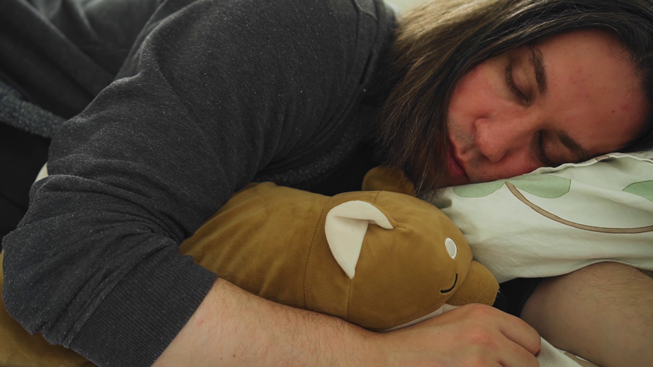 一个男人抱着一个小玩具躺在床上休息。近距离射击视频下载