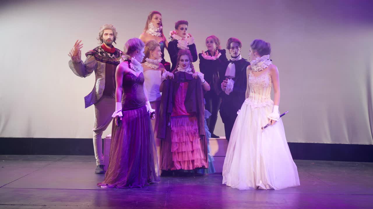 宽镜头女演员穿着公主装在舞台上模仿剑战，演员们欢呼雀跃。白人美女在剧院里扮演角色表演现代戏剧，吓得逃跑。视频下载