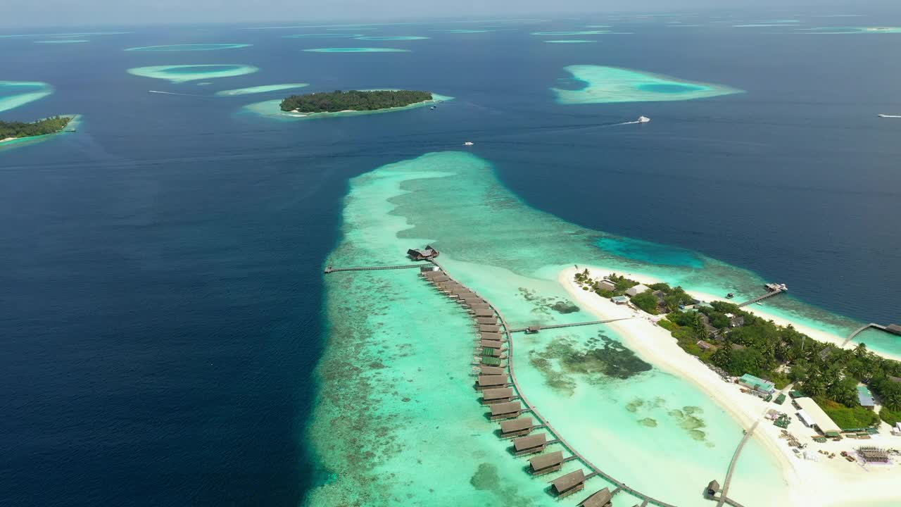 空中拍摄的岛屿与旅游度假村与水上平房，无人机在阳光明媚的日子里向后飞越海洋-马尔代夫的thulushoo视频下载