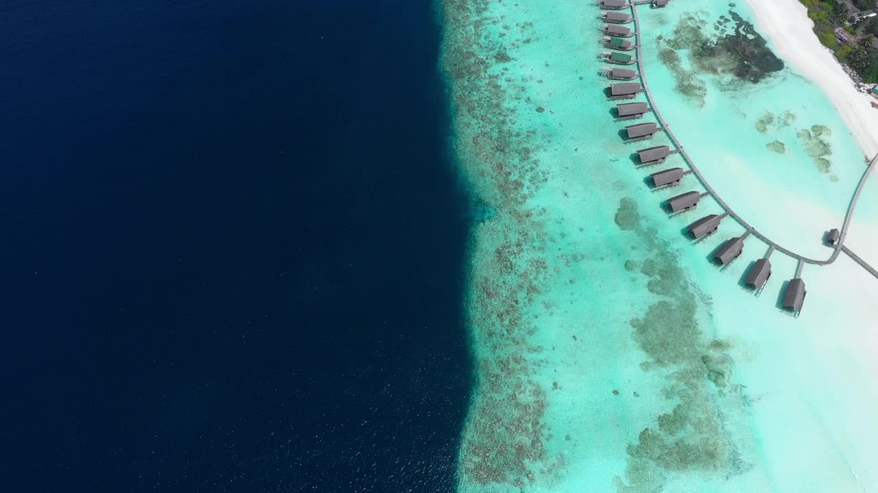 空中拍摄的水上平房在阳光明媚的一天，无人机飞过蓝绿色和蓝色的海洋-马尔代夫thulushoo视频素材