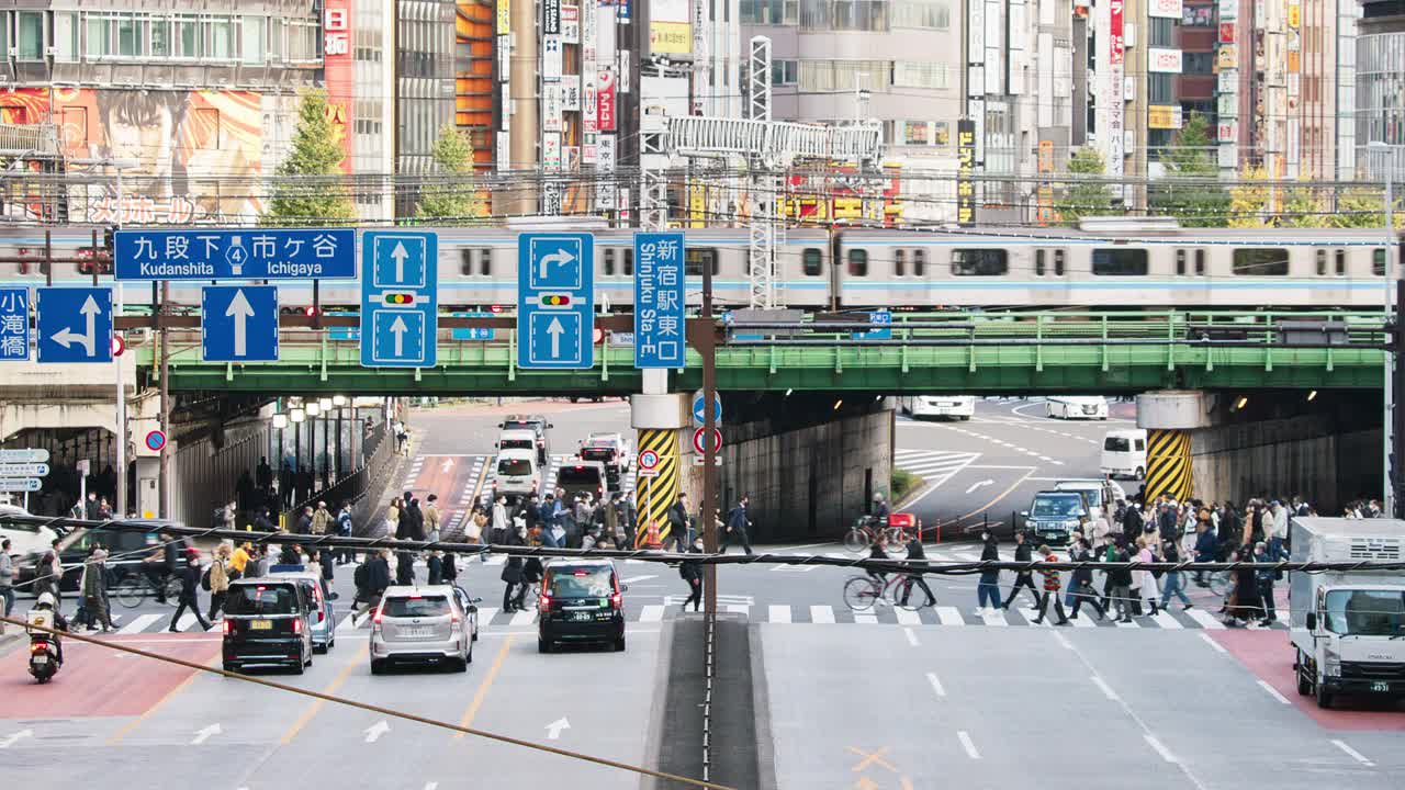 汽车、公共汽车交通运输在道路十字路口，地铁列车在高架轨道上，日本人在日本东京新宿区走过十字路口。亚洲交通，亚洲城市生活。视频下载