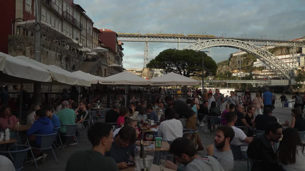 繁忙的水边咖啡馆和餐厅，日落时分的杜罗河和多姆路易斯一世桥，波尔图，北，葡萄牙，欧洲视频下载