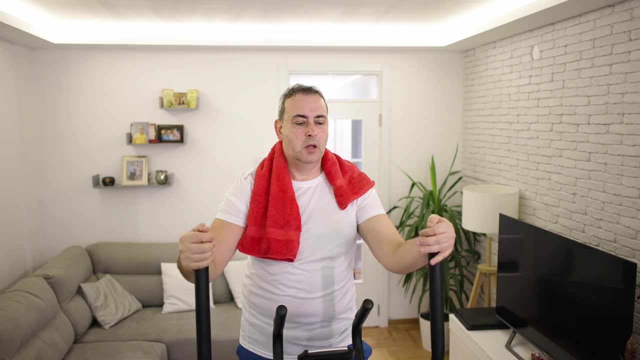 中年男子在客厅的北欧滑雪健身机上锻炼时汗流浃背视频下载