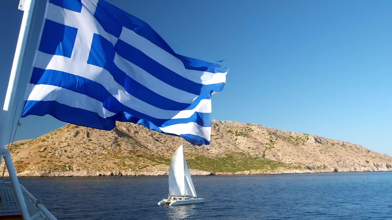 希腊国旗在一个岛屿和一艘经过的帆船上飘扬，这是希腊的象征视频下载
