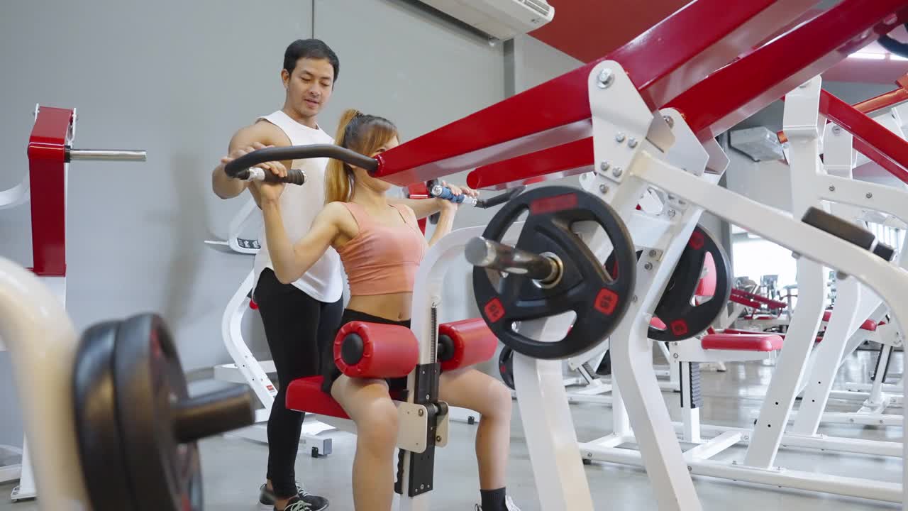 美丽的亚洲女人在健身房与她的教练进行长时间的杠杆肩压练习后，在健身机上小睡片刻视频下载